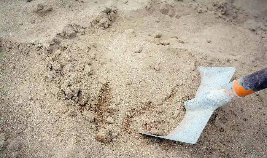 Auf dem Bild ist typischer, hellbrauner Sand zu sehen in etwas gröberer Körnung. Ein Spaten schaufelt, von rechts kommend, etwas ab.