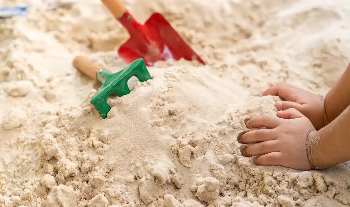 Spielsand, Bild zeigt Kinderhände und Spielzeugschaufel im Sand