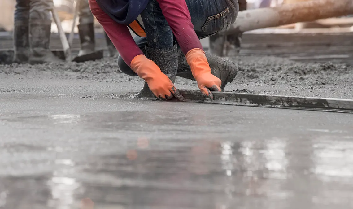 Betontankstelle für Beton, Estrich und Mörtel zeigt Person, die hockend Beton glatt zieht auf einer Baustelle.
